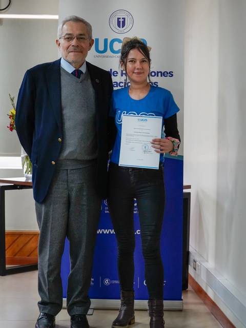 Una mujer y un hombre posan juntos sosteniendo un certificado en un evento académico.