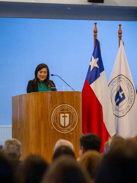 Una mujer habla desde un podio en un evento formal rodeada de banderas chilenas.