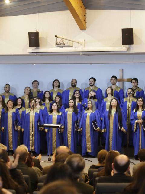 Un coro vestido con túnicas azules actúa en un evento formal frente a un público atento.