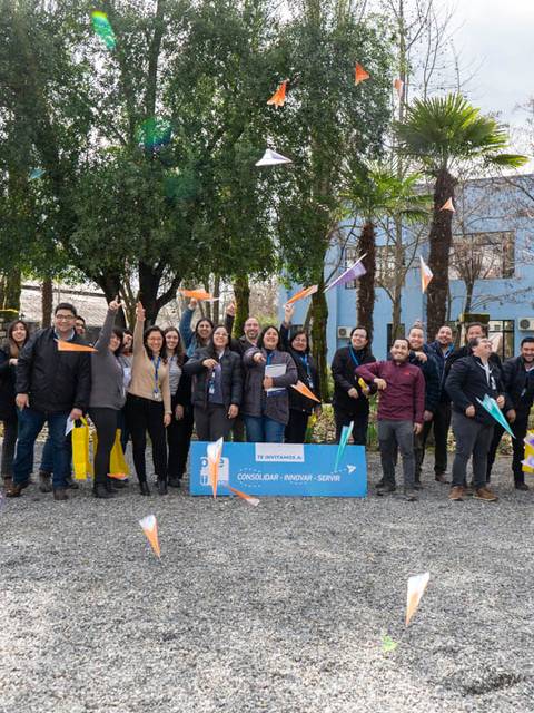 Un grupo de personas sonrientes posa en un entorno al aire libre con árboles y edificios de fondo.
