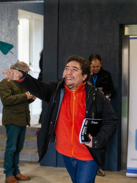 Un grupo de personas en un evento, mientras un hombre lanza un avión de papel con entusiasmo.