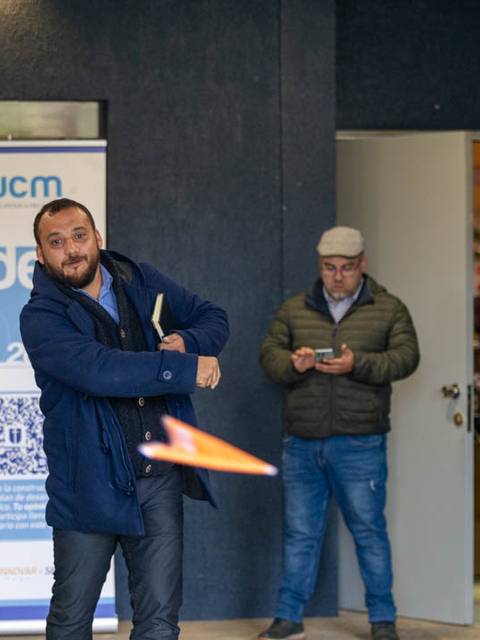 Un hombre lanza un objeto en un espacio abierto mientras otro hombre observa desde una puerta.