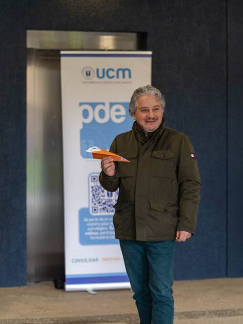 Un hombre sonriente sostiene un avión de papel en un evento organizado por la UCM.
