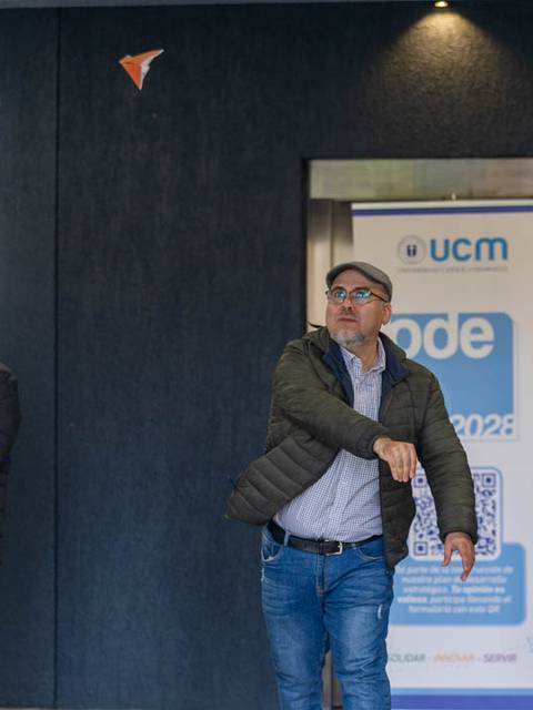 Un hombre lanza un avión de papel mientras otros esperan en la entrada de un edificio.