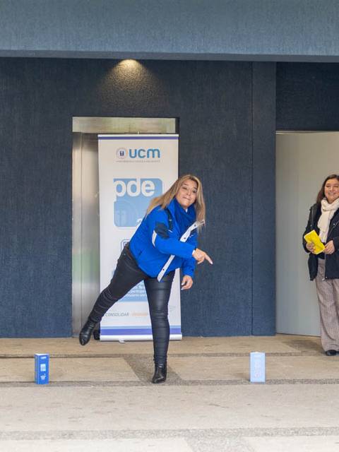 Una mujer lanza un objeto en un evento organizado por la UCM mientras un grupo de personas observa.