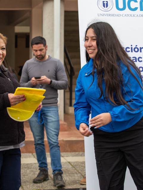 Un grupo de personas interactúa en un evento universitario, destacando a dos mujeres sonrientes.