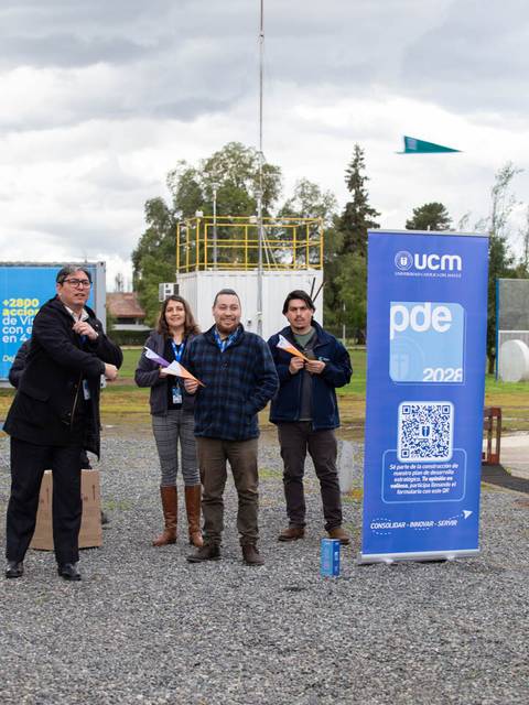Cuatro personas posando frente a un banner de UCM en un entorno al aire libre.