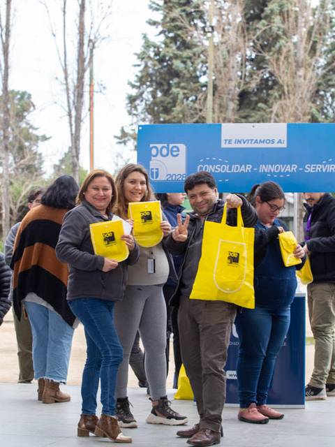 Un grupo de personas sonrientes sostiene bolsas amarillas en un evento al aire libre.