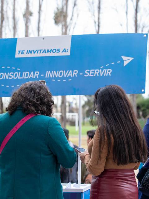 Un grupo de personas observa un cartel informativo en un evento al aire libre.