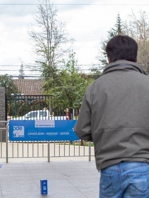 Tres personas observan un evento al aire libre frente a un cartel promocional.