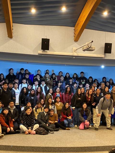 Un gran grupo de personas posando en un escenario con banderas chilena y de otros organismos en un ambiente interior.