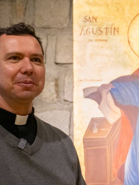 Un hombre sonriente de pie junto a una pintura de San Agustín.
