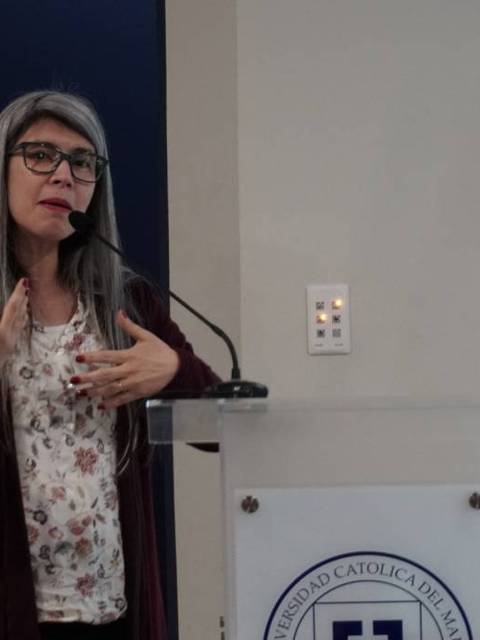 Una mujer de cabello largo y gris está hablando en un micrófono frente a una audiencia.