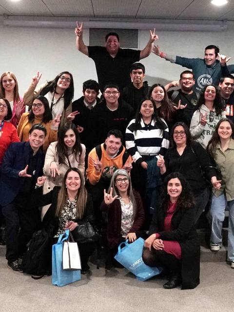 Un grupo grande de personas posando juntas con gestos de paz en un evento.