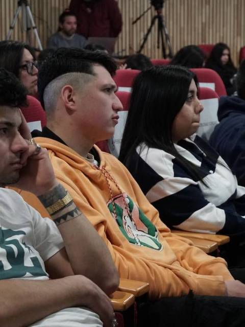 Un grupo de personas sentadas en un auditorio, escuchando atentamente una presentación.
