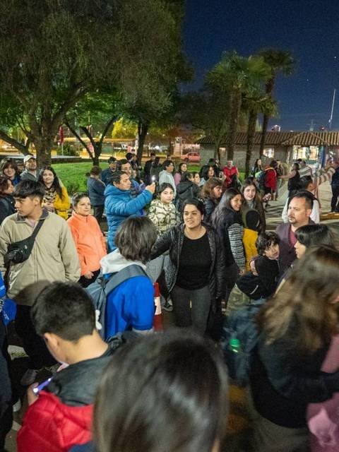 Un grupo grande de personas se encuentra reunido en un lugar durante la noche, posiblemente esperando para abordar un autobús.