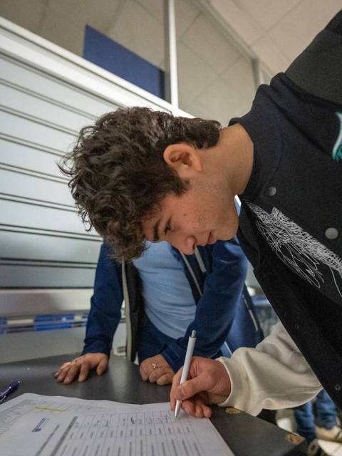 Un joven está escribiendo en un formulario en una mesa.