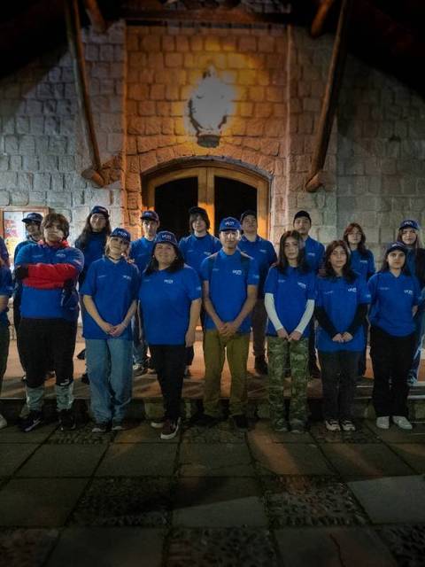 Un grupo de personas vestidas con camisetas azules se encuentra en un ambiente exterior, frente a un edificio antiguo.