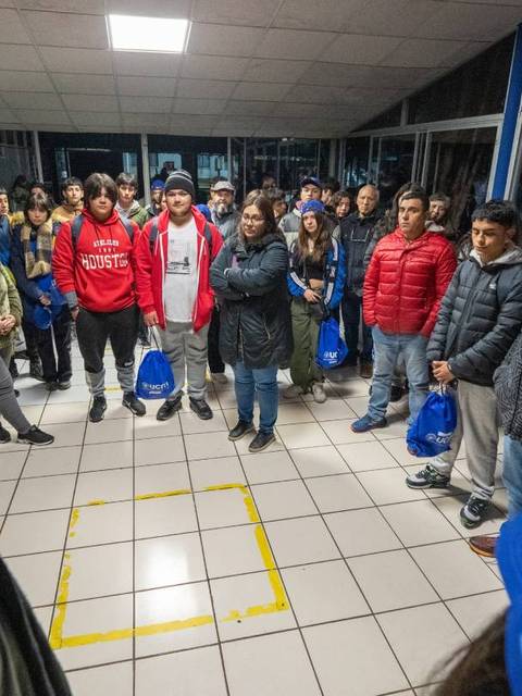 Un grupo de personas se encuentra reunido en un espacio cerrado, observando atentamente a un orador en el centro de un cuadrado marcado en el suelo.