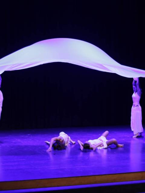Un grupo de bailarines en el escenario sosteniendo una tela blanca mientras realizan una coreografía.