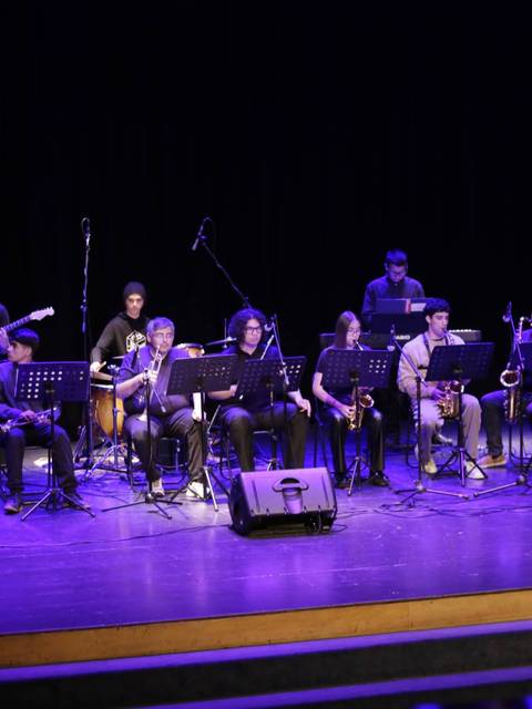 Un grupo de músicos se presenta en un escenario iluminado mientras tocan instrumentos variados.