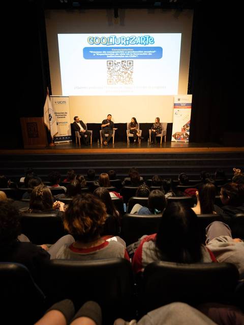 Una conferencia está teniendo lugar en un auditorio con un público atento.