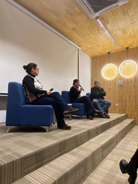 Un panel de discusión en un auditorio con tres participantes sentados en sillas frente a un público atento.