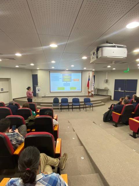 Una presentación en una sala con asientos rojos y un proyector mostrando información en la pantalla.