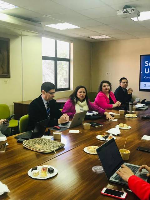 Una reunión en una sala con varias personas alrededor de una mesa con laptops y comida.