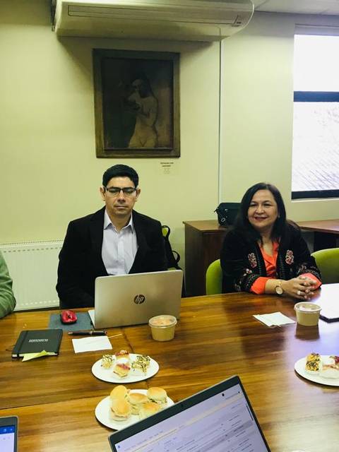 Un grupo de personas se encuentra en una reunión en una sala con una mesa de madera, laptops y café.