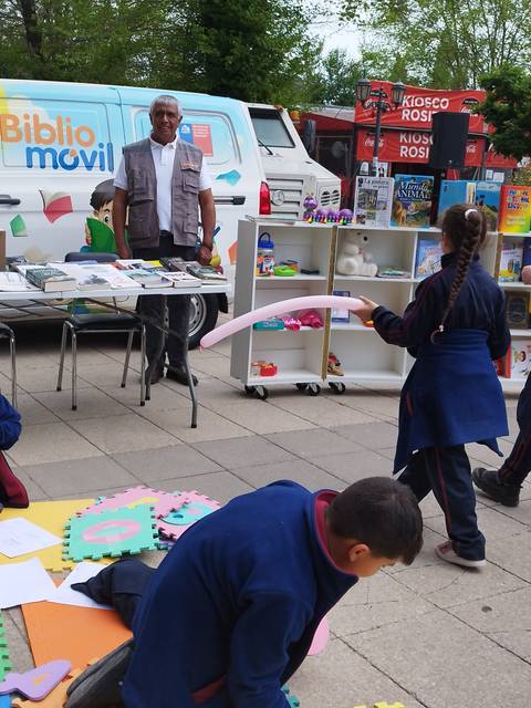 Una feria literaria al aire libre con niños jugando y un bibliomóvil de fondo.