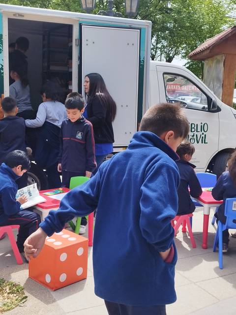 Un grupo de niños juega y aprende alrededor de un vehículo de biblioteca móvil en un ambiente al aire libre.