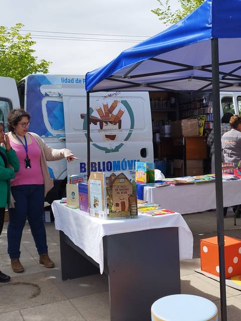 Un evento comunitario con un puesto de libros al aire libre y varias personas interactuando.