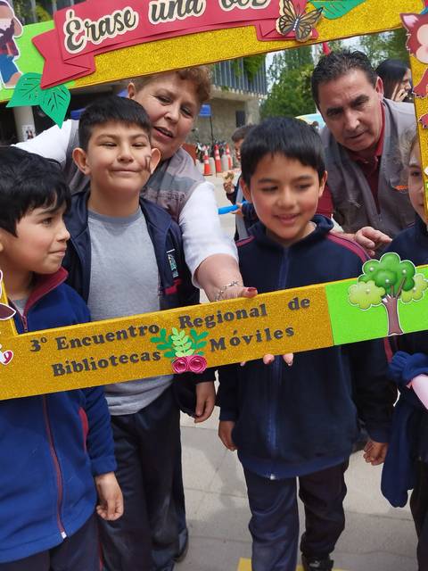 Un grupo de niños y adultos participan en un encuentro de bibliotecas móviles, sonriendo y sosteniendo un marco decorativo.