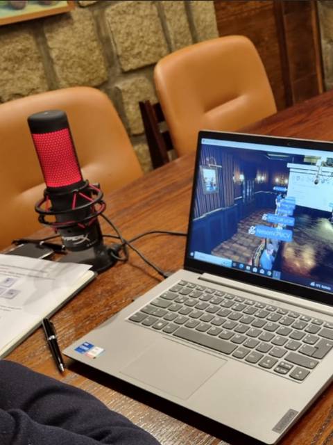 Un hombre observa una pantalla de computadora mientras trabaja, con un micrófono rojo y documentos sobre la mesa.