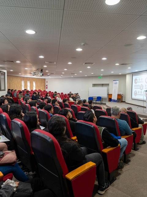 Una sala de conferencias llena de estudiantes prestando atención a un orador en un escenario.