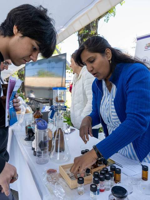 Una mujer presenta un proyecto sobre el tratamiento de agua a un joven en un evento educativo al aire libre.