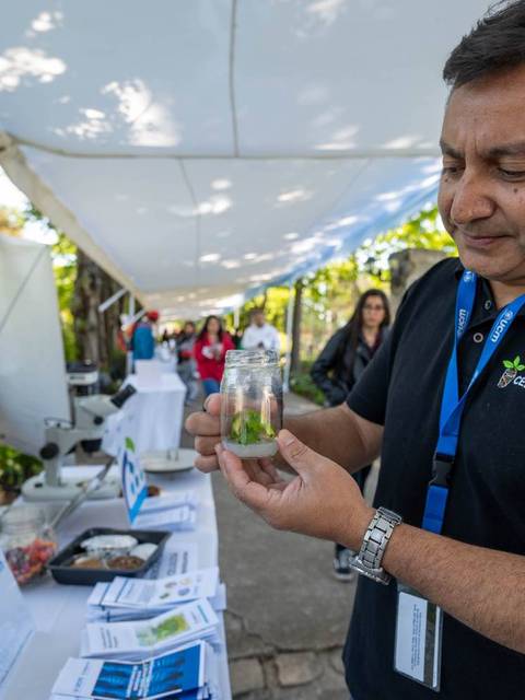 Un hombre sostiene un frasco con plantas en un evento al aire libre.
