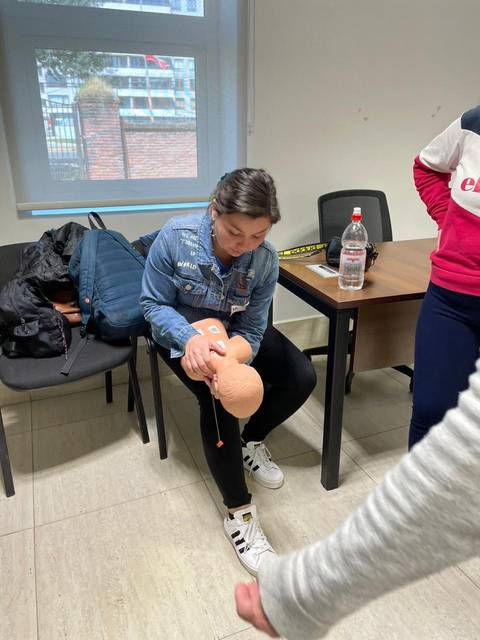 Una mujer está sentada en una silla, manipulando un modelo anatómico humano en un entorno de clase.