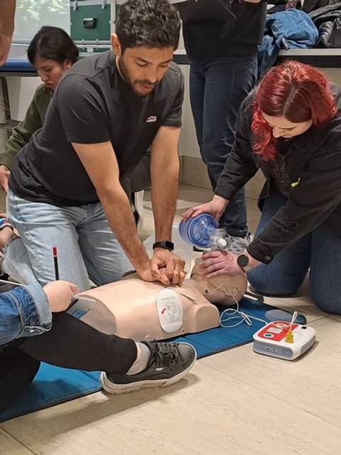 Un grupo de personas está practicando técnicas de resucitación en un maniquí en un aula.