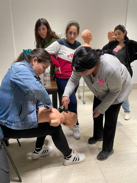 Un grupo de mujeres está practicando resucitación en un muñeco de cpr durante un taller.