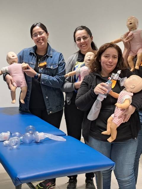 Un grupo de personas sostiene muñecos en un aula con una mesa azul.