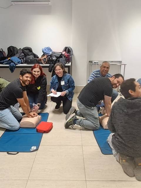 Un grupo de personas en una sala práctica de primeros auxilios realizando maniobras de reanimación cardiopulmonar (RCP) sobre muñecos.