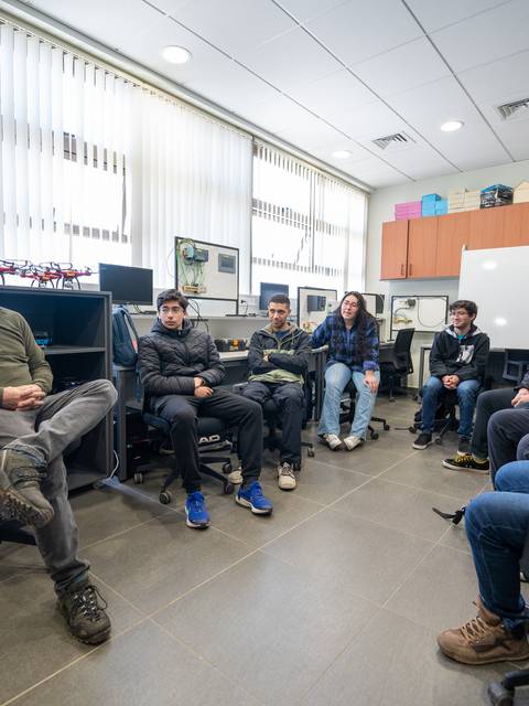 Un grupo de estudiantes y un profesor discutiendo en un aula equipada con computadoras.