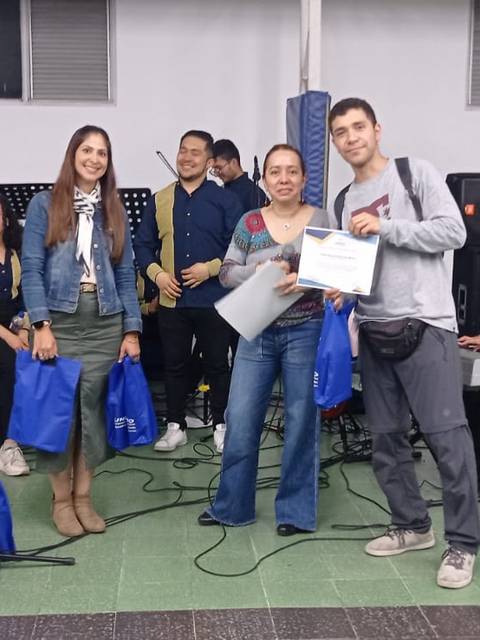 Un grupo de personas celebrando un evento con música, donde dos de ellas sostienen premios y bolsas azules.