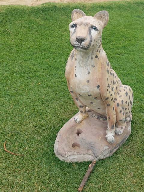 Una escultura de un guepardo sentada en un paisaje verde.