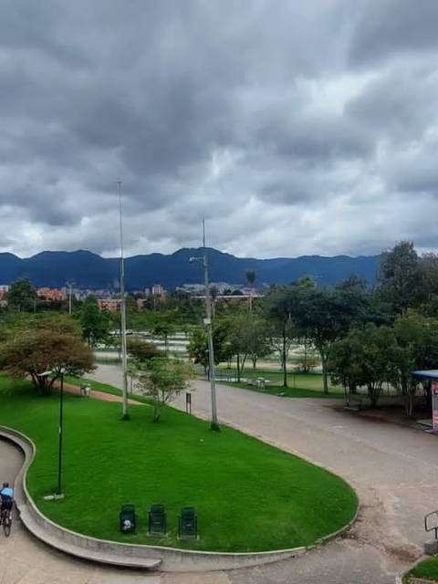 Una vista panorámica de un parque con árboles, caminos y montañas al fondo bajo un cielo nublado.