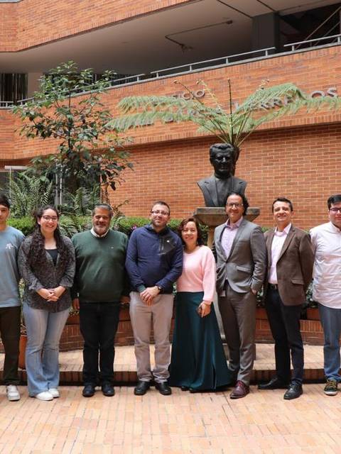 Un grupo de personas posando en un entorno académico con una estatua al fondo.