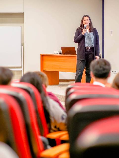 Una presentadora habla frente a un público en un auditorio.