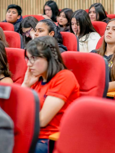 Un grupo de estudiantes sentados en un auditorio, atentos a una presentación.